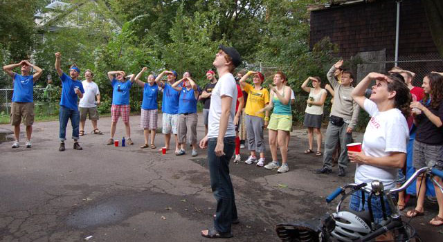 a group of people stand around outside looking up (at something we can't see)